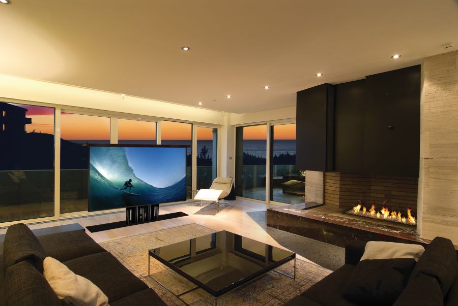 A living area overlooking the ocean, with a couch, fireplace, and hidden TV rising from the ground. 