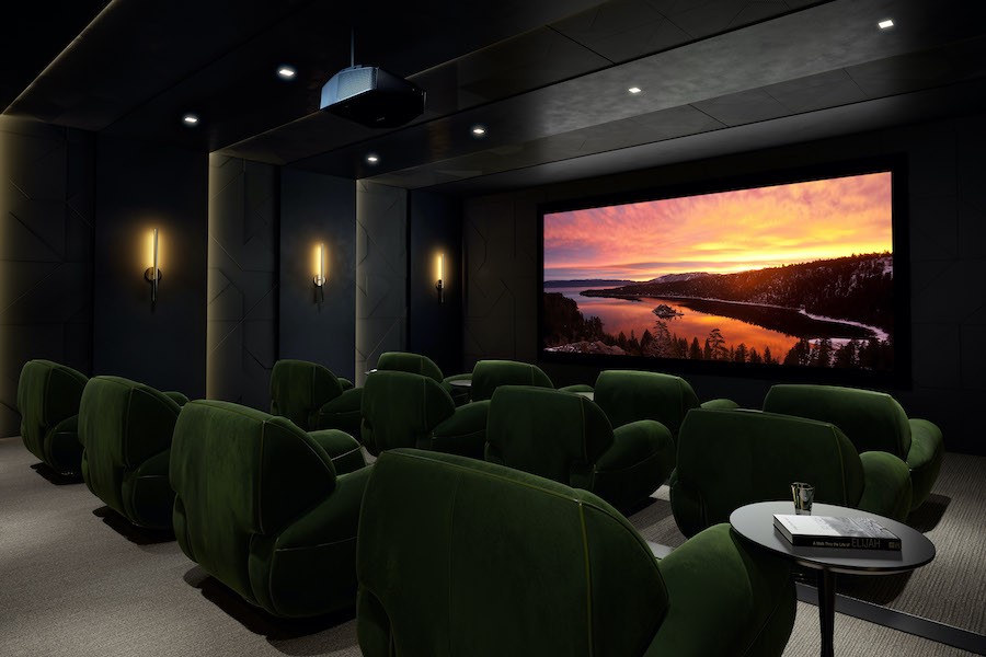 A home theater with plush, green seats and a projected image of a sunset on the screen.